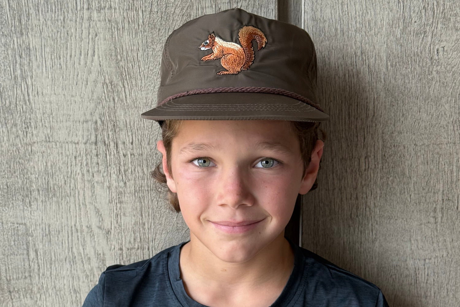 Person wearing a cap with a squirrel on it, lying on a textured surface