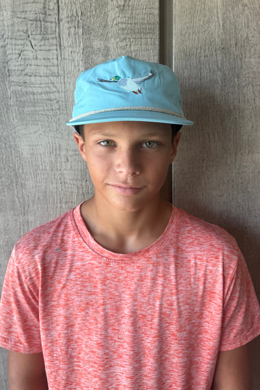 Teen boy wearing a blue cap with flying mallard duck on it, red shirt against a wooden wall