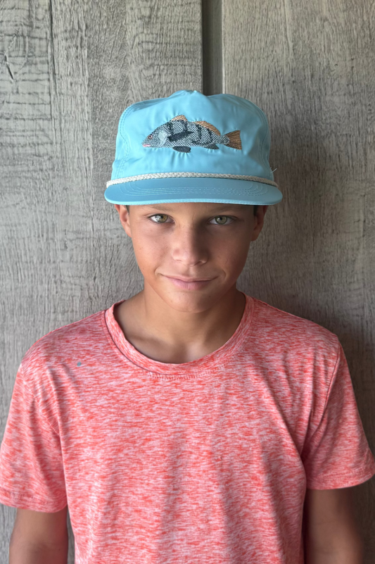 Child wearing a blue cap with a fish design against a wooden background